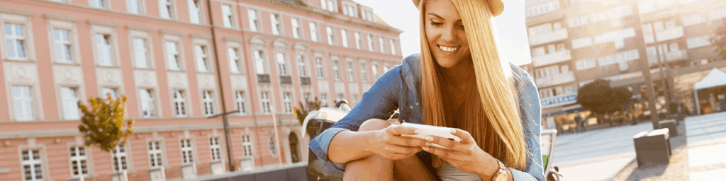 Young woman smiling while using her smartphone outdoors in a European city square on a sunny day