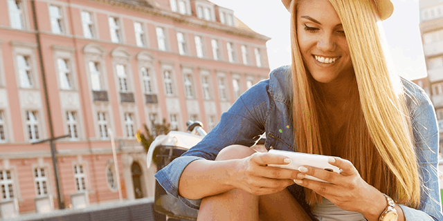 Young woman smiling while using her smartphone outdoors in a European city square on a sunny day
