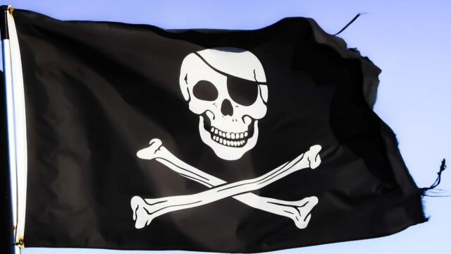Jolly Roger pirate flag with skull and crossbones waving against a blue sky