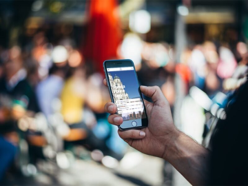 Person holding a smartphone showing the Samoa Police Service website in a busy outdoor setting