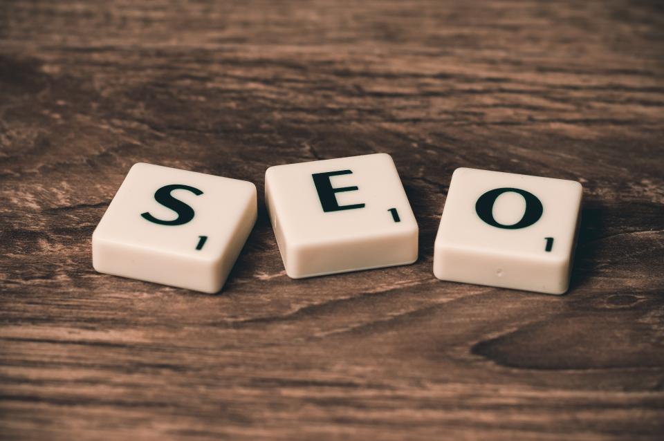 Three Scrabble tiles spelling SEO on a wooden surface, representing search engine optimisation concepts