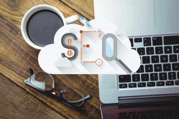 SEO letters inside a cloud graphic overlaid on a laptop and coffee cup on a wooden desk