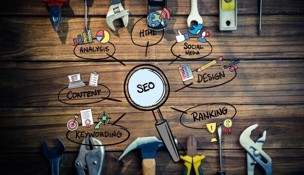 Magnifying glass labelled SEO on a wooden workbench with speech bubbles showing SEO components: content, keywords, ranking, design, HTML, and social media