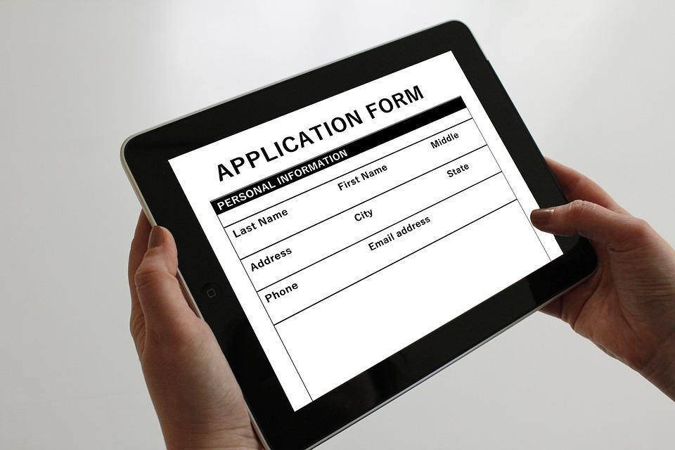 Hands holding a tablet displaying a job application form with personal information fields