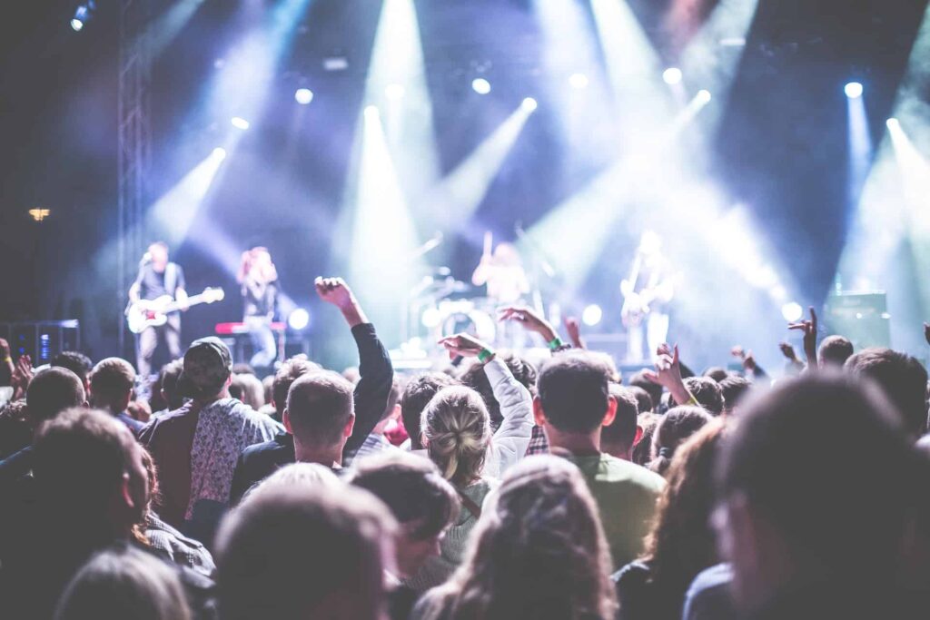 Concert crowd with raised hands facing a band on a brightly lit stage, illustrating live event ticket sales