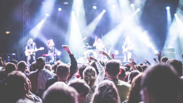 Concert crowd with raised hands facing a band on a brightly lit stage, illustrating live event ticket sales