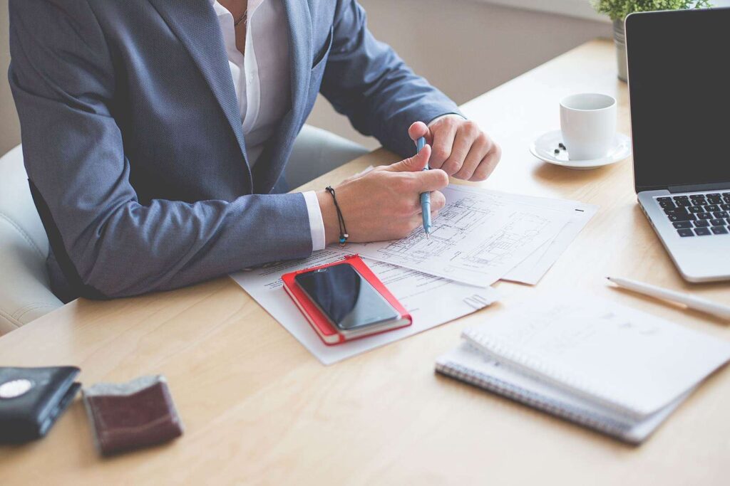 Business professional reviewing documents and wireframes at a desk with a laptop and coffee