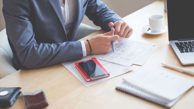 Business professional reviewing documents and wireframes at a desk with a laptop and coffee