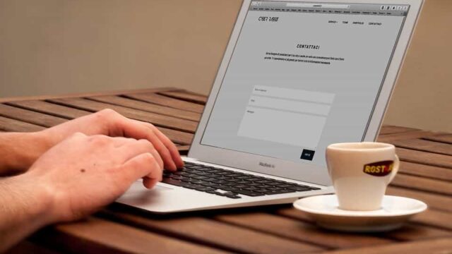 Hands typing on a MacBook Air with a website contact page open, coffee cup beside it