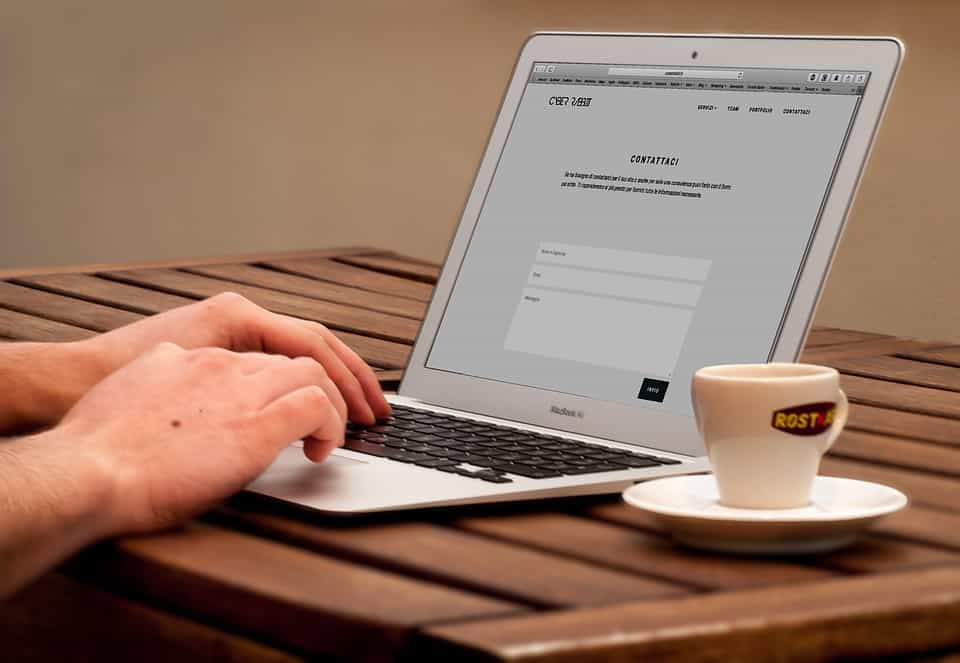 Hands typing on a MacBook Air with a website contact page open, coffee cup beside it