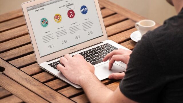 Person browsing a website on a MacBook Air at a wooden table with a coffee cup nearby