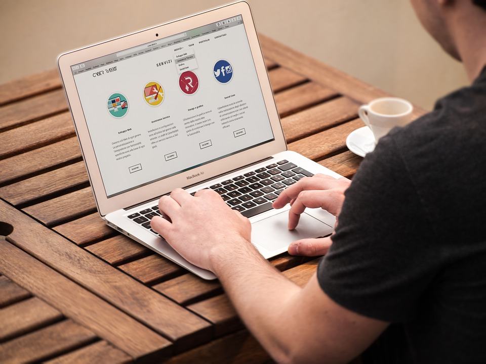 Person browsing a website on a MacBook Air at a wooden table with a coffee cup nearby
