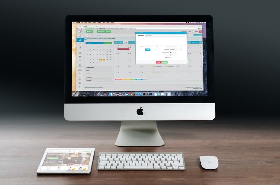 iMac desktop showing a web application calendar dashboard with a tablet and keyboard on a desk