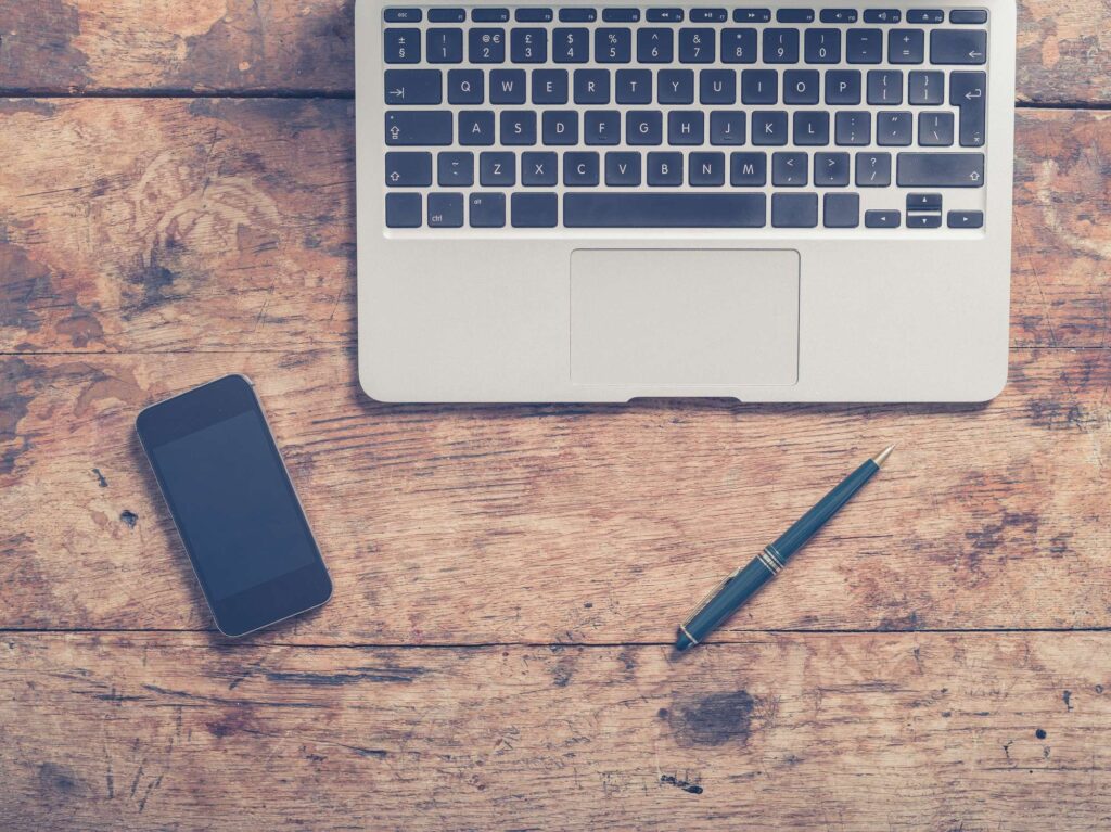 Laptop, smartphone and pen arranged on a wooden desk, used as the featured image for the why you should learn SEO article