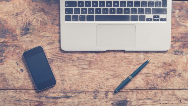 Laptop, smartphone and pen arranged on a wooden desk, used as the featured image for the why you should learn SEO article