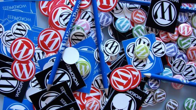 Collection of colourful WordPress logo badges, stickers, and pencils spread across a table