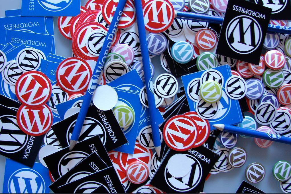 Collection of colourful WordPress logo badges, stickers, and pencils spread across a table